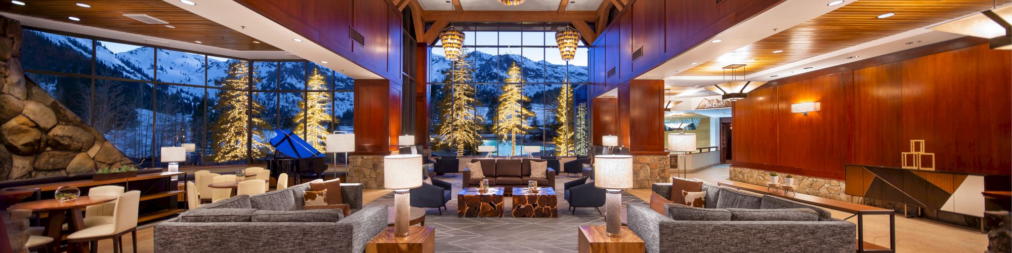 A modern and spacious lobby with large windows showcasing a snowy landscape. Features cozy seating, wooden accents, and elegant chandeliers.