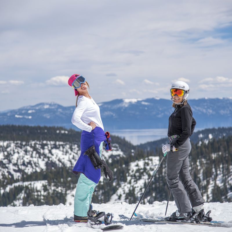 Two people are standing on a snowy mountain with ski equipment, posing in front of a scenic landscape.