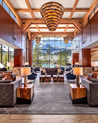 A spacious, luxurious lobby with elegant chandeliers, large windows showcasing mountains, and cozy seating areas. Modern, warm, and inviting atmosphere.