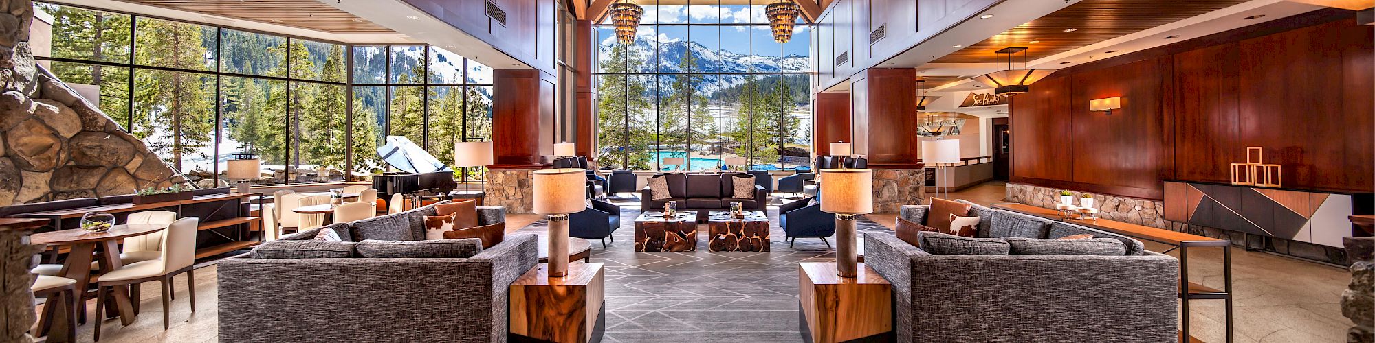The image shows a spacious, luxurious hotel lobby with modern furniture, large windows offering mountain views, and elegant lighting fixtures.