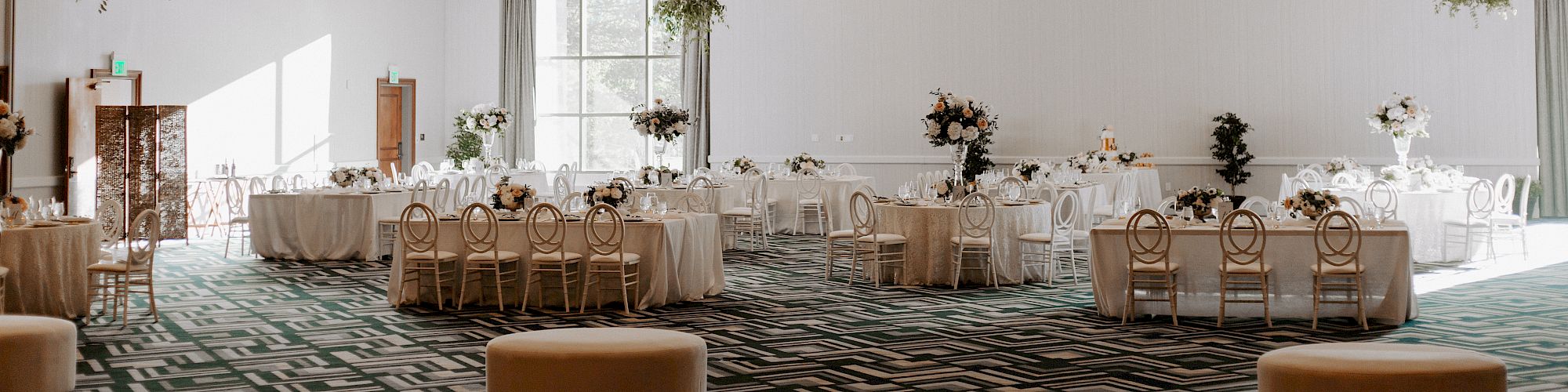 This image shows an elegant event hall setup with round tables and chairs, white drapery, floral centerpieces, and soft lighting.