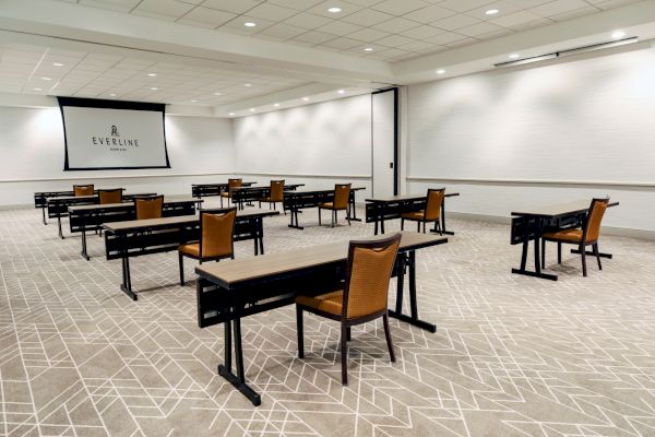 A conference room with spaced-out tables and chairs facing a projector screen displaying the Everline logo.