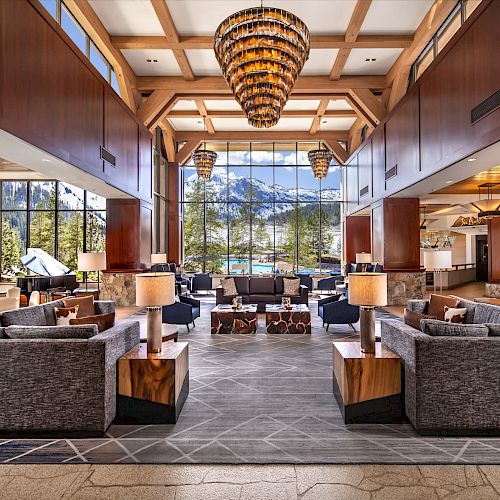 A spacious, modern hotel lobby with large windows, comfortable seating areas, wooden accents, and a stunning chandelier hanging from a high ceiling.