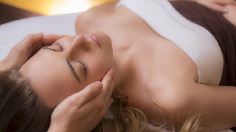 A person is receiving a relaxing head or facial massage while lying down, with their eyes closed and a calm expression.